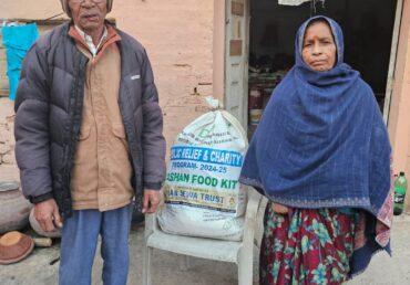 Old couple with Jan Sewa Trust food kit standing outside their home