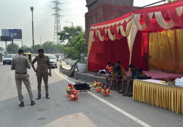 Two policemen standing by a road with a red tent and seated men nearby