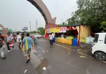 People walking near a food stall on a street with a banner, Jan Sewa Trust