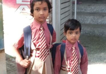 Two young children in school uniforms and backpacks standing outside a building