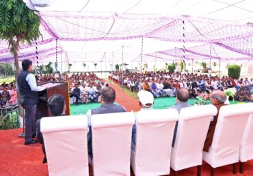 Jan Sewa Trust-NGO event with speaker at podium, audience in chairs, large tent